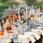 Luxury wedding reception, dining table setup with decoration on rustic wooden table. Dishes, cutlery, napkins and accessories, dry plants, glasses and candles on table for guests, flat lay, outdoor