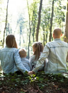 SeminarhausPartner - Familienfreizeiten - Eltern halten Händchen - sitzen mit Kindern auf Baumstamm im Wald